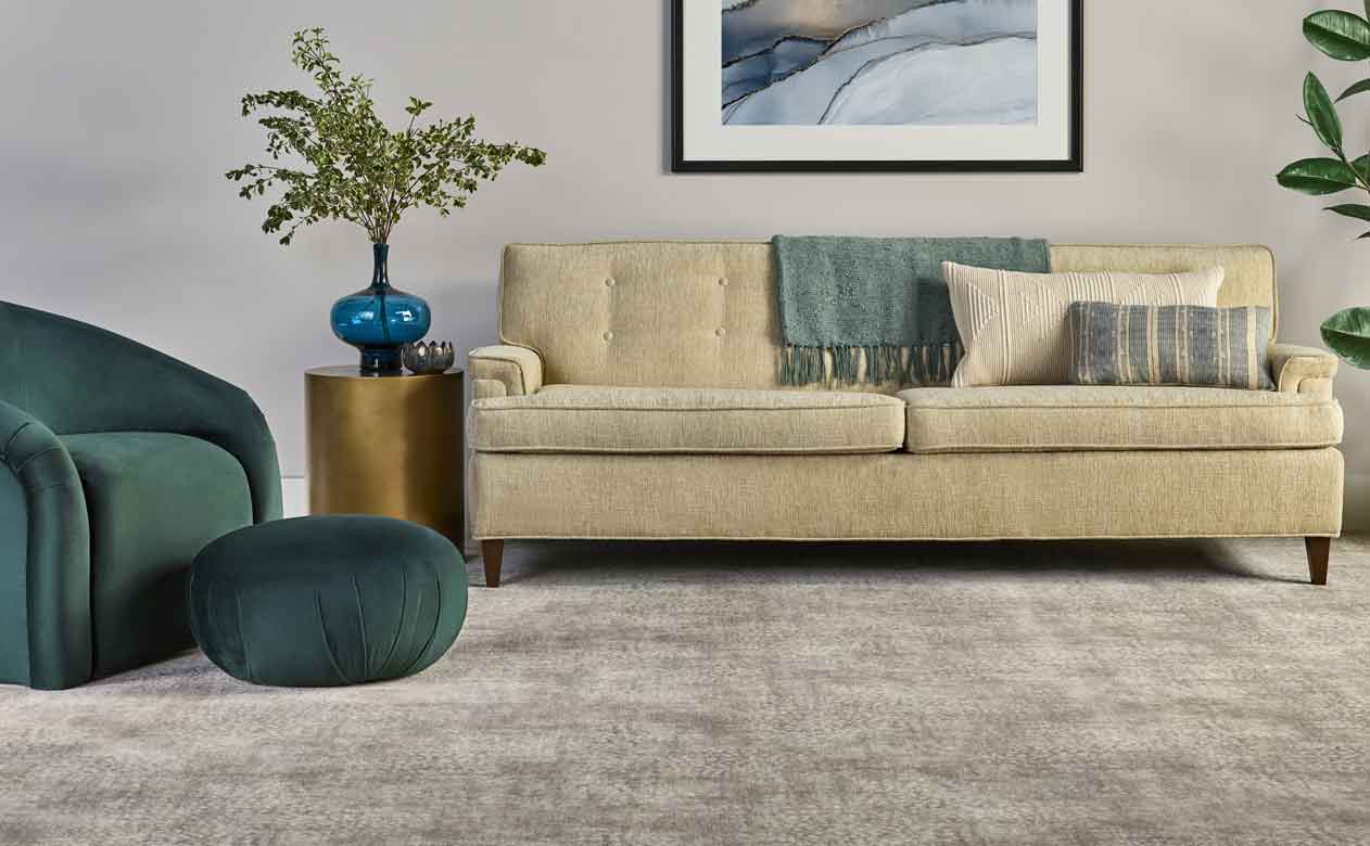 Living room with velvet green chair and ottoman with beige couch and greige patterned carpet